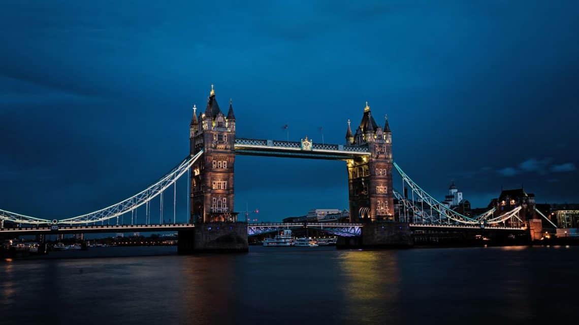 Večerný pohľad na osvetlený Tower Bridge v Londýne s tmavomodrou oblohou v pozadí.